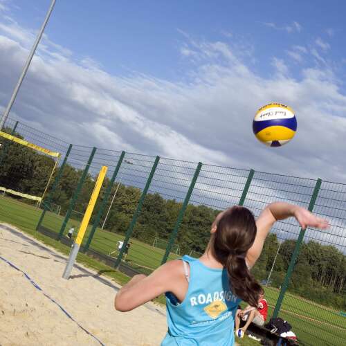 Ein Mädchen spielt Beachvolleyball an einem sonnigen Tag. Sie schlägt den Ball über das Netz auf dem Sandplatz.
